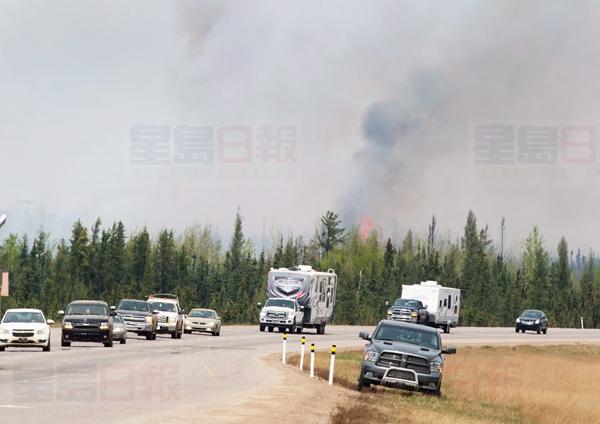 A convoy of evacuees drive past wildfires that are still burning out of control south of Fort McMurray, Alta., on Saturday, May 7, 2016. THE CANADIAN PRESS/Ryan Remiorz