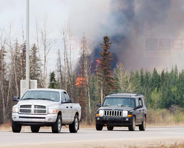 A convoy of evacuees drive past wildfires that are still burning out of control south of Fort McMurray, Alta., on Saturday, May 7, 2016. THE CANADIAN PRESS/Ryan Remiorz