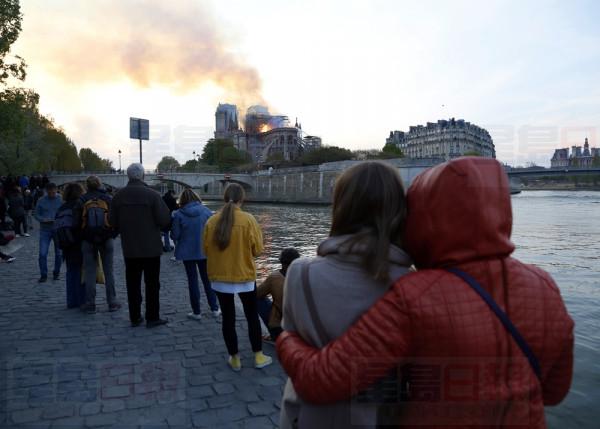 People watch as flames and smoke rise from Notre Dame cathedral as it burns in Paris, Monday, April 15, 2019. Massive plumes of yellow brown smoke is filling the air above Notre Dame Cathedral and ash is falling on tourists and others around the island that marks the center of Paris. (AP Photo/Thibault Camus)