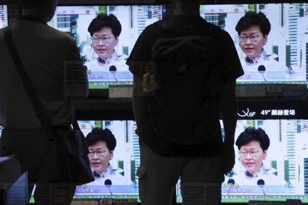 Residents watch a broadcast of Chief Executive Carrie Lam speaking at a press conference held in Hong Kong on Saturday, June 15, 2019. Lam said she will suspend a proposed extradition bill indefinitely in response to widespread public unhappiness over the measure, which would enable authorities to send some suspects to stand trial in mainland courts. (AP Photo/Vincent Yu)