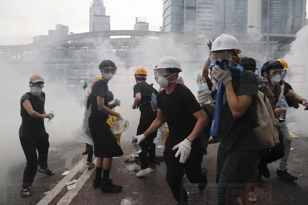 Demonstrators react to a cloud of tear gas near the Legislative Council in Hong Kong, Wednesday, June 12, 2019. Hong Kong police fired tear gas and high-pressure water hoses against protesters who had massed outside government headquarters Wednesday in opposition to a proposed extradition bill that has become a lightning rod for concerns over greater Chinese control and erosion of civil liberties in the semiautonomous territory. (AP Photo/Kin Cheung)