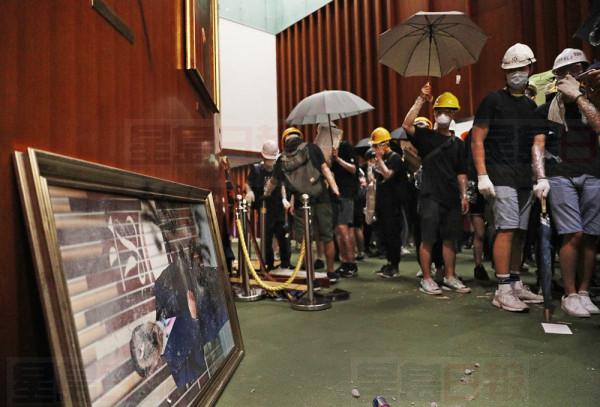 Protesters holding umbrellas walk past a damaged Legco chairman picture at the Legislative Chamber after break in to protest against the extradition bill in Hong Kong, Monday, July 1, 2019. The extradition law has aroused concerns that this legislation would undermine the city's independent judicial system as it allows Hong Kong to hand over fugitives to the jurisdictions that the city doesn't currently have an extradition agreement with, including mainland China, where a fair trial might not be guaranteed. (AP Photo/Vincent Yu)