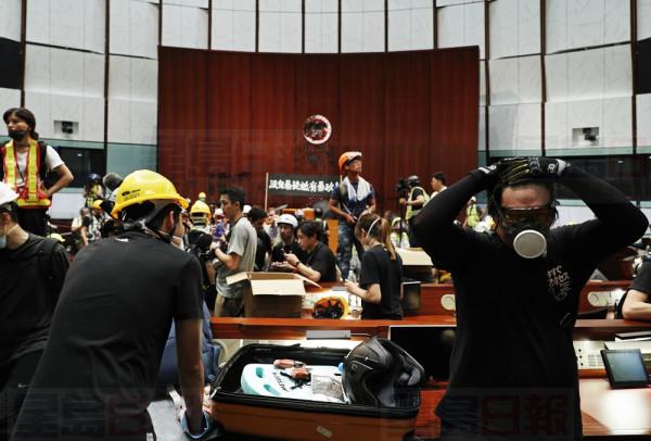 A protester adjusts his mask in front of a defaced Hong Kong logo after break in at the Legislative Chamber to protest against the extradition bill in Hong Kong, Monday, July 1, 2019. The extradition law has aroused concerns that this legislation would undermine the city's independent judicial system as it allows Hong Kong to hand over fugitives to the jurisdictions that the city doesn't currently have an extradition agreement with, including mainland China, where a fair trial might not be guaranteed. (AP Photo/Vincent Yu)