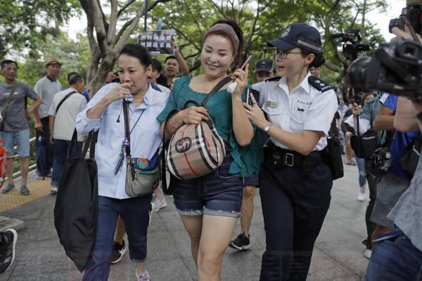 A Chinese street performer, center, is escorted by police officers as she is surrounded by protestors at the Tuen Mun Park, in Hong Kong, Saturday, July 6, 2019. Hundreds of protesters gathered in northwest Hong Kong Tun Mun, protesting against mainland Chinese singers causing nuisance to the local neighborhood. The extradition protest sparked Hong Kong netizen to line more protest during the weekend, with focus on some local conflicts between mainland Chinese and Hong Kongers. (AP Photo/Kin Cheung)