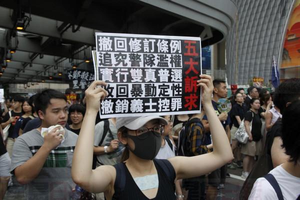 A protester holds up a card with demands for the government in Hong Kong on Sunday, July 7, 2019. Thousands of people, many wearing black shirts and some carrying British flags, were marching in Hong Kong on Sunday, targeting a mainland Chinese audience as a month-old protest movement showed no signs of abating. (AP Photo/Andy Wong)