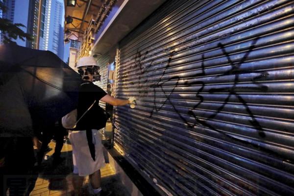 A protester sprays the words "Against Extradition to China" on the shutters of a pharmacy that sells to mainland customers, in Hong Kong, Saturday, July 13, 2019. Several thousand people marched in Hong Kong on Saturday against traders from mainland China in what is fast becoming a summer of unrest in the semi-autonomous Chinese territory. (AP Photo/Kin Cheung)