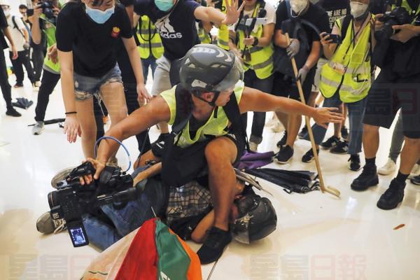A journalist tries to protect a policeman lies on the floor after he being attacked by protesters inside a shopping mall in Sha Tin District in Hong Kong, Sunday, July 14, 2019. Police in Hong Kong have fought with protesters as they broke up a demonstration by thousands of people demanding the resignation of the Chinese territory's chief executive and an investigation into complains of police violence. (AP Photo/Kin Cheung)