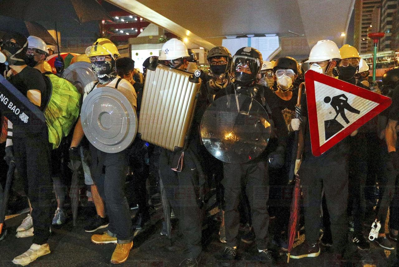 Protesters carrying home-made shields face off with riot policemen on a street in Hong Kong, Sunday, July 21, 2019. Hong Kong police have thrown tear gas canisters at protesters after they refused to disperse. Hundreds of thousands of people took part in a march Sunday to call for direct elections and an independent investigation into police tactics used during earlier pro-democracy demonstrations. Police waved a black warning flag Sunday night before lobbing the canisters into a crowd of protesters. (AP Photo/Bobby Yip)