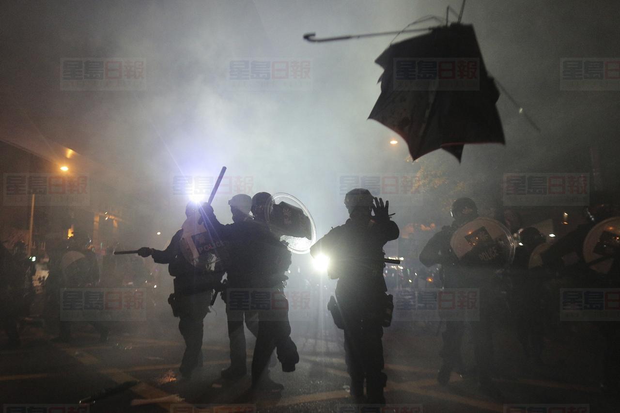 A broken umbrella flies by near riot police, during confrontation with protesters in Hong Kong Sunday, July 21, 2019. Hong Kong police launched tear gas at protesters Sunday after a massive pro-democracy march continued late into the evening. The action was the latest confrontation between police and demonstrators who have taken to the streets to protest an extradition bill and call for electoral reforms in the Chinese territory. (Andy Lo/HK01 via AP)