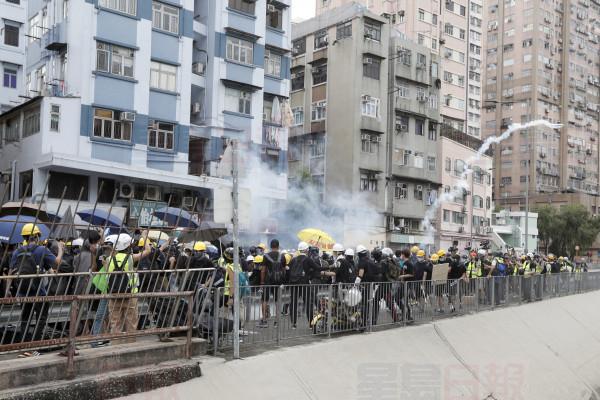Protesters react to tear gas as they face off with riot police at the entrance to a village at Yuen Long district in Hong Kong Saturday, July 27, 2019. Police fired tear gas at protesters who defied authorities' warnings not to march in a neighborhood where six days earlier a mob apparently targeting demonstrators brutally attacked people in a train station. (AP Photo/Bobby Yip)