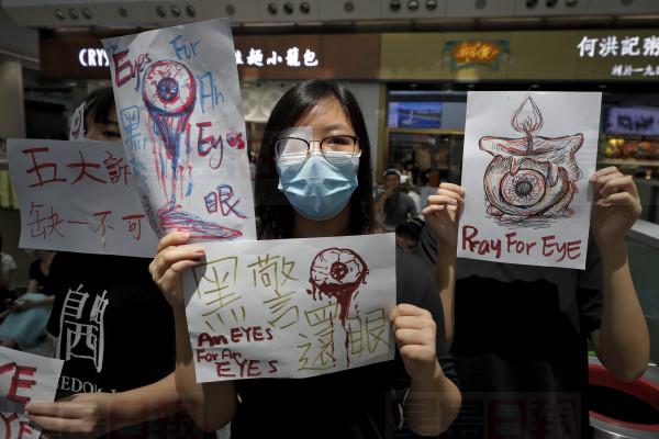 People hold signs which read " Black Police, Return eye," bottom center, during a protest at the arrival hall of the Hong Kong International airport in Hong Kong, Monday, Aug. 12, 2019. It is reported that police shot a woman in the eye with a projectile Sunday night during confrontations between protesters and police. (AP Photo/Vincent Thian)