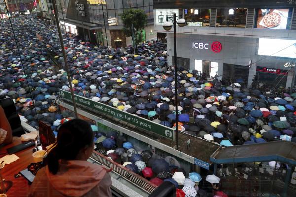 A woman watches demonstrators march along a street in Hong Kong, Sunday, Aug. 18, 2019. Heavy rain fell on tens of thousands of umbrella-ready protesters as they started marching from a packed park in central Hong Kong, where mass pro-democracy demonstrations have become a regular weekend activity. (AP Photo/Vincent Yu)
