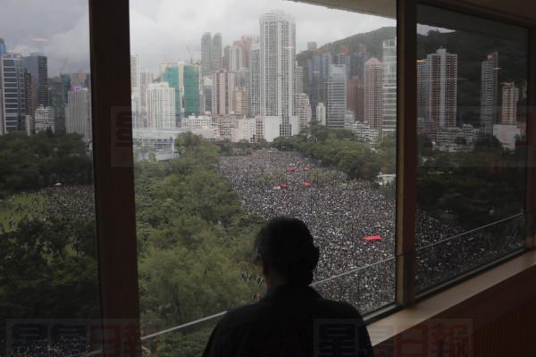 A person stands near a window overlooking a protest on Victoria Park in Hong Kong on Sunday, Aug. 18, 2019. Thousands of people streamed into a park in central Hong Kong on Sunday for what organizers hope will be a peaceful demonstration for democracy in the semi-autonomous Chinese territory. (AP Photo/Kin Cheung)