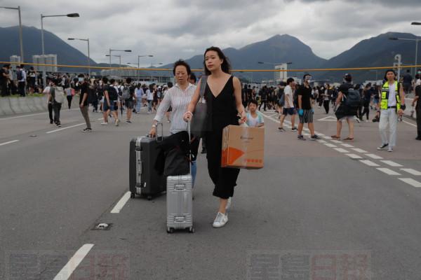 Passengers walk to airport as pro-democracy protestors blocked a road outside the airport in Hong Kong, Sunday, Sept.1, 2019. Train service to Hong Kong's airport was suspended Sunday as pro-democracy demonstrators gathered there, while protesters outside the British Consulate called on London to grant citizenship to people born in the former colony before its return to China. (AP Photo/Kin Cheung)