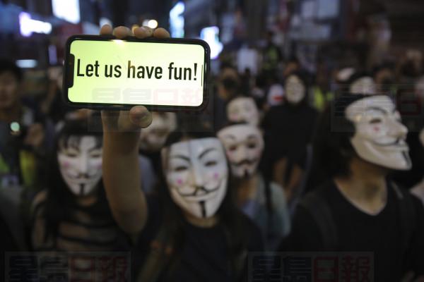 A person wearing a Guy Fawkes mask holds a smartphone with a message reading "Let us have fun!" as people gather on a street in Hong Kong, Thursday, Oct. 31, 2019. Hong Kong authorities are bracing as pro-democracy protesters urged people on Thursday to celebrate Halloween by wearing masks on a march in defiance of a government ban on face coverings. (AP Photo/Kin Cheung)